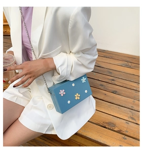Blue square chain bag with 3D daisy flowers shown on a white blazer outfit