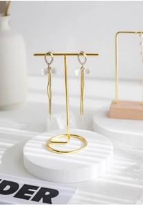 Detail of gold tassel earrings with rhinestone bow on a minimalist display stand