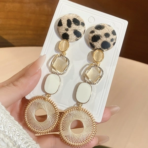 Détail de boucles d'oreilles bohèmes avec imprimé léopard, cadre strass et pompon en fil doré