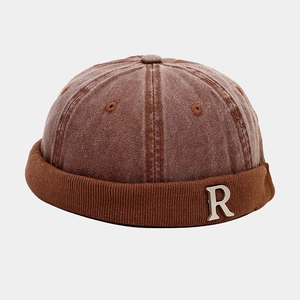 Detail of retro brown brimless hat with corduroy edge and silver metal R letter charm