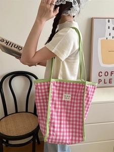 Pink and white checkered canvas tote bag with green handles shown on shoulder by model