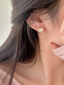 Close-up of heart-shaped shell earrings in gold frame worn on model earlobe