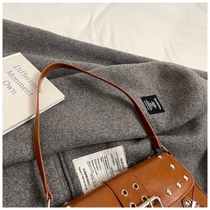Detailed close-up of brown punk shoulder bag with silver metal studs and eyelet straps