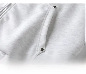 Detailaufnahme der Seitentasche mit Nieten und Metallreißverschluss am grauen Hoodie