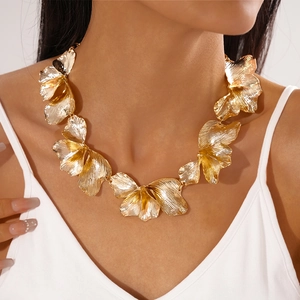 Close-up of a bold golden metallic flower necklace worn by a model in a studio setting