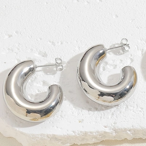 Detailed view of silver thick C-shaped brass earrings on a textured stone background