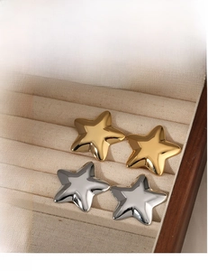 Close-up of 3D star stud earrings in gold and silver finish on a beige velvet surface