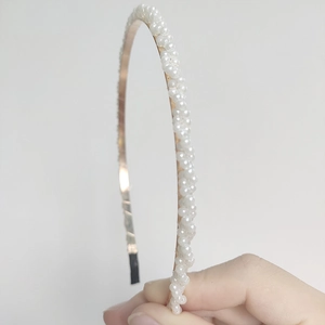 Detail showing handcrafted white faux pearls woven on a golden metal headband base