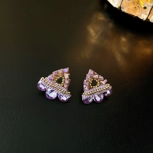 Close-up of elegant triangle earrings with purple crystals and gold beads on black texture