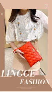 Close-up of a red quilted clutch bag with gold brand plate and matching wristlet strap