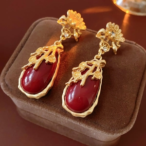 Macro shot of vintage gold flower earrings with red oval gemstones on brown velvet