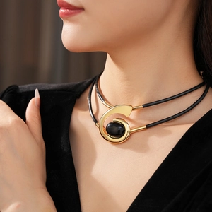 Detail of gold chain woven with black leather and an oval gemstone on model