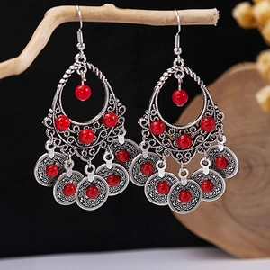 Macro shot of vintage silver earrings with red beads hanging on a rustic wooden branch