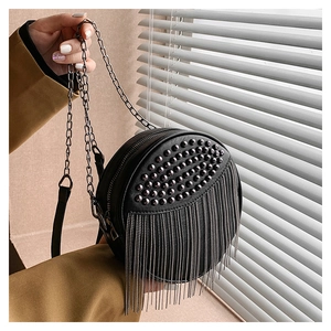 Detail of black round crossbody bag featuring metallic studs and hanging chain tassels