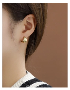 Macro shot of gold-plated triple row C-shaped hoop earrings worn by a model