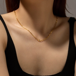 Close-up of golden paperclip link necklace with a blue gemstone pendant on a model
