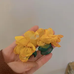 Detailed close-up of yellow gauze flower earrings with green leaf tassels being held