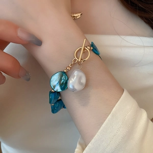 Detail of blue shell bracelet with gold T-bar clasp and white baroque pearl pendant