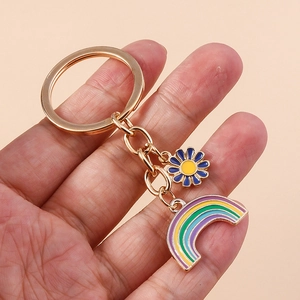 Detail of a gold enamel keychain featuring a colorful rainbow and a daisy flower pendant