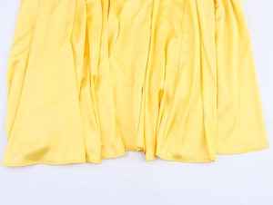 Close-up of the flowing yellow satin skirt hem showing smooth texture and elegant drape