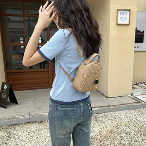 Outdoor shot of a beige quilted PU leather mini backpack with a gold cat charm
