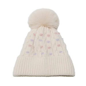 Detalle de gorro de punto trenzado crema con pompones de colores y pompón de piel sintética
