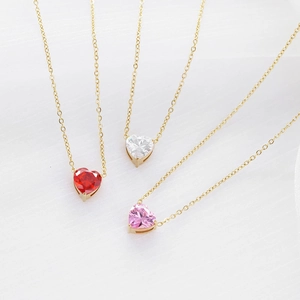 Tres collares dorados con colgantes de corazón rojos, blancos y rosas sobre tela