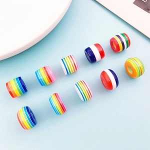Macro shot of twelve colorful rainbow striped resin barrel beads arranged on light blue background