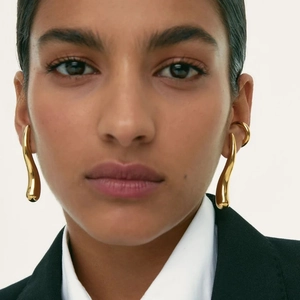 Close-up detail of smooth 18K gold teardrop earrings worn on a model with metallic shine