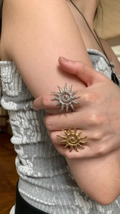 Detail of sun-shaped rings with wavy rays in gold and silver finish on model's hand