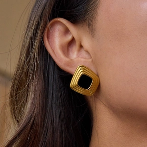 Gros plan d'élégantes boucles d'oreilles carrées dorées avec insert noir sur un mannequin
