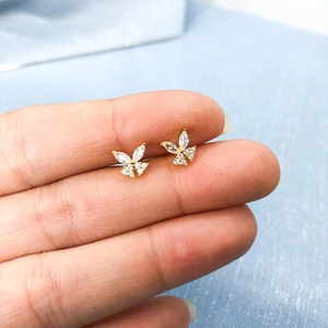 Macro shot of tiny gold butterfly stud earrings with sparkling cubic zirconia on finger