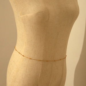 Detailed view of a layered gold beaded waist chain on a mannequin for summer fashion