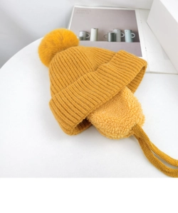 Detailed shot of yellow knitted hat with soft lamb wool earflaps and large pompom