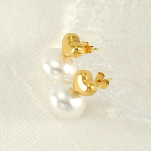 Detail of heart-shaped gold studs with large lustrous pearls on white textured fabric