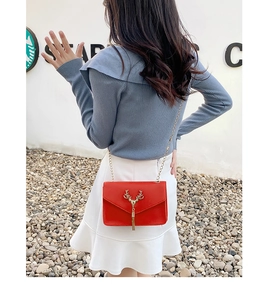 Red crossbody bag with gold deer head clasp and chain strap shown on model shoulder
