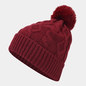 Detail of dark red cable knit beanie featuring a fluffy faux fur pompom and ribbed cuff