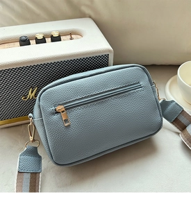 Detail of light blue pebble leather crossbody bag with wide striped strap and zip pocket