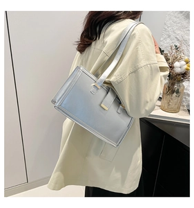 Side view of a silver metallic rectangle tote bag worn by a model in a modern interior
