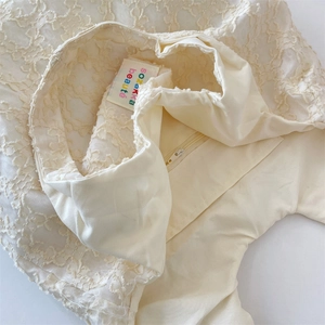 Detail of floral lace texture and interior brand embroidery on the cream handbag