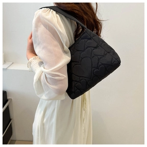 Détail d'un sac à bandoulière noir avec broderie motif cœur porté par un mannequin en robe