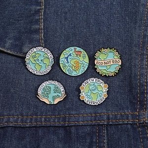 Detail of five eco-friendly enamel pins with environmental slogans on blue denim fabric