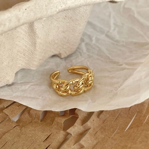Detailed view of a gold chain-link adjustable ring on minimalist paper background