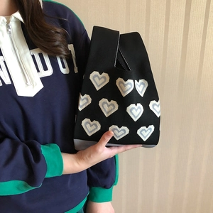 Detail of hand-held black knitted tote bag featuring blue and white heart patterns