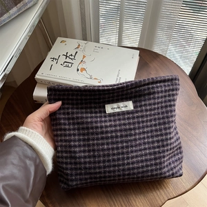 Close-up of a hand holding a purple plaid woolen cosmetic pouch with simple wish label