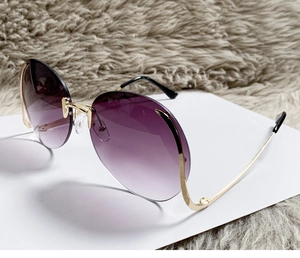 Detail view of purple gradient lenses and gold metal frames of rimless sunglasses