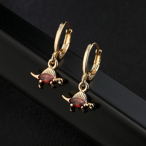 Golden dinosaur earrings with red oval gemstones on black textured surface