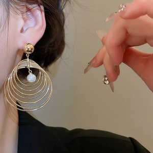 Detail of layered gold hoop earrings with white pearl drop on female model wearing