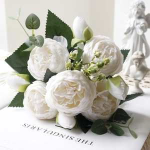 Close-up of white silk peony bouquet with lush green leaves next to vintage sculptures
