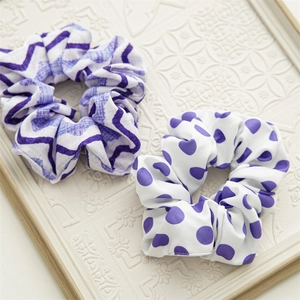 Detail showing two fabric scrunchies with purple wavy and polka dot patterns on white cloth